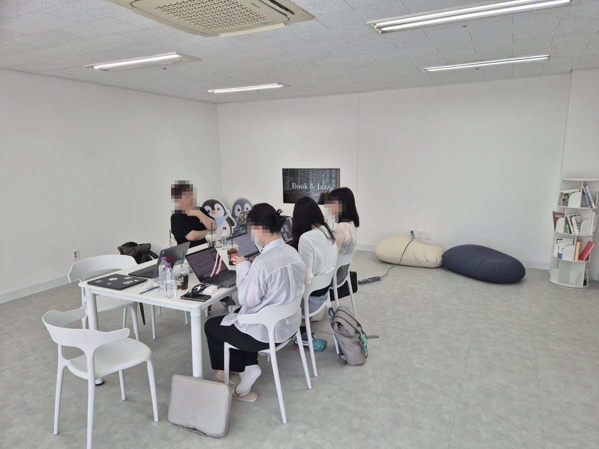 흰 테이블에 노트북을 펴고 둘러앉아 각자 작업하며 이야기를 나누는 참가자들. 얼굴은 모자이크 처리했다